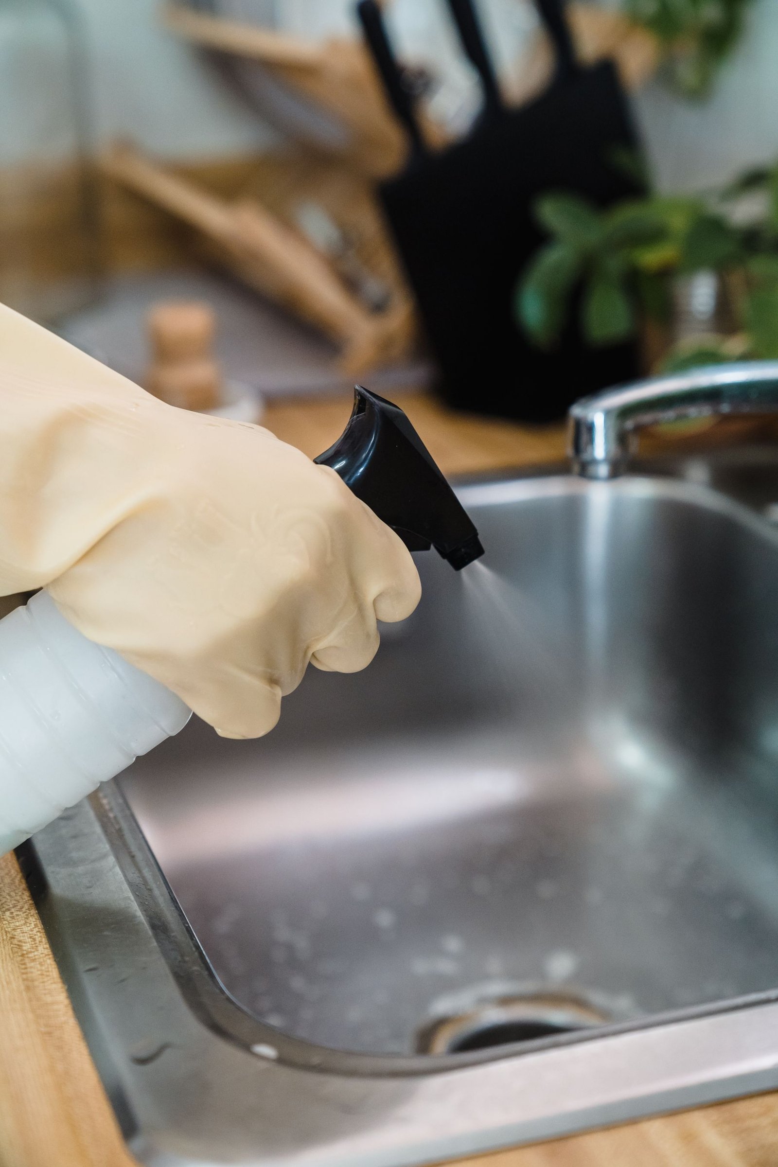 Gloved hand cleaning a kitchen sink with a spray bottle